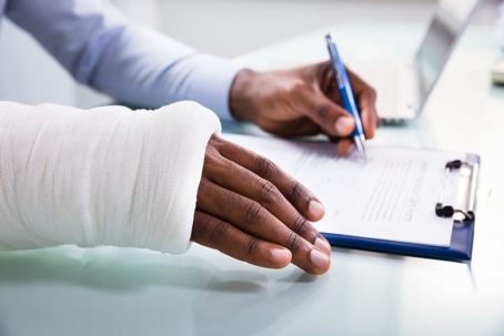 Person signing medical forms on a clipboard while having a cast on their right arm.